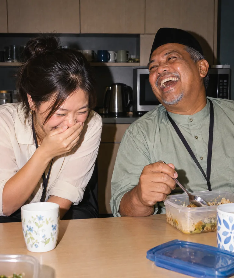 Two colleagues bursting into laughter over lunch in the office pantry